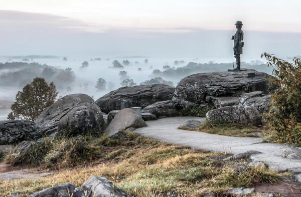A bronze statue stands on a rockface overlooking a foggy hillside