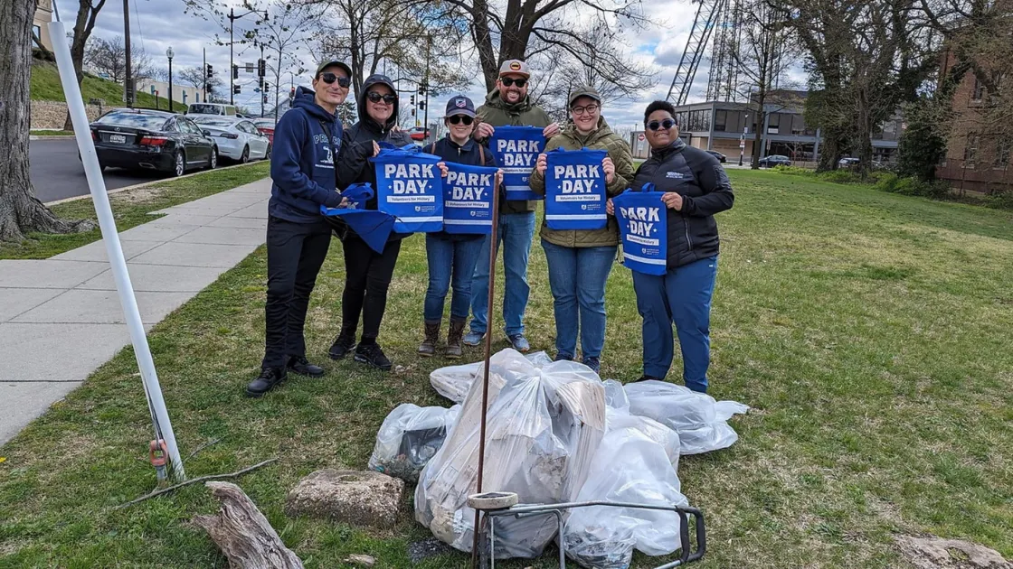 Volunteers hold up Park Day tote bags and stand in front of trash they collected at Fort Stevens