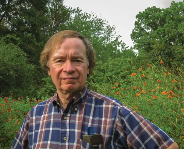 A photograph of a man standing in front of trees and wildflowers on a battlefield